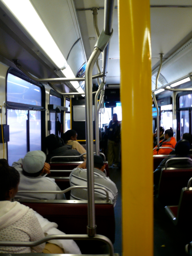 Innenansicht eines Busses: Sitzreihen mit vertikalen Stangen an einigen von ihnen.