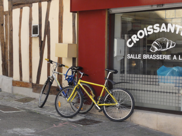 Zwei Fahrräder nebeneinander auf einem Gehweg vor einem Geschäft mit einer Glaswand und einem Objekt links von den Fahrrädern.