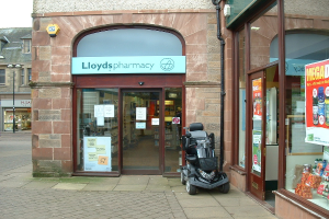 Eine Apotheke mit einem davor geparkten Fahrzeug und einem Gebäude in der linken Ecke.