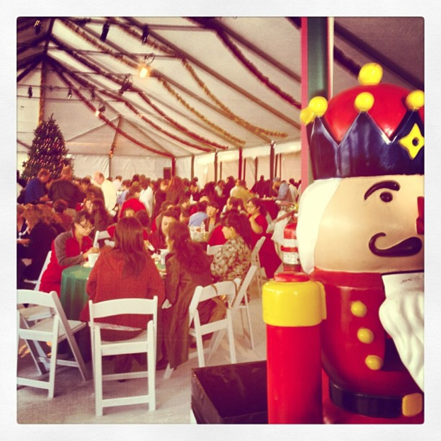 Eine Gruppe von Menschen, die Weihnachten in einer Hütte feiern, mit einem geschmückten Baum, weißen Stühlen, einem roten Spielzeug-Sicherheitswächter und einer schwarzen Krone.