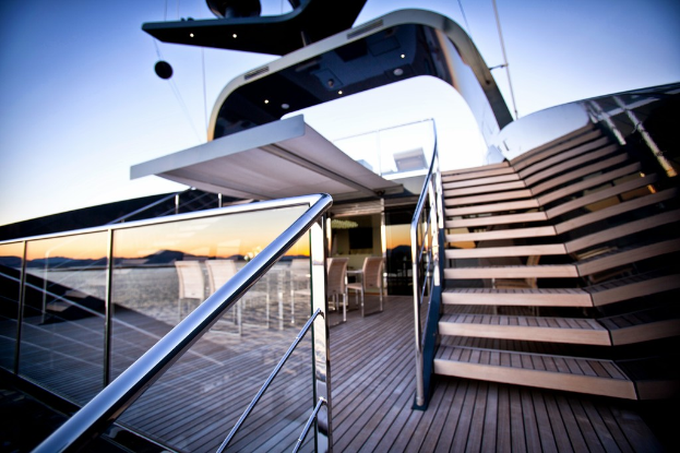 Ein modernes Glashaus mit Treppe auf der rechten Seite, Stühle um einen Tisch auf der linken Seite und ein Glasgeländer auf der linken unteren Seite.