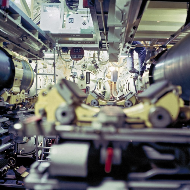 Ein Mann steht auf einer Maschine in einem Raum voller verschiedener Maschinen und Gegenstände und scheint an der Maschine zu arbeiten.