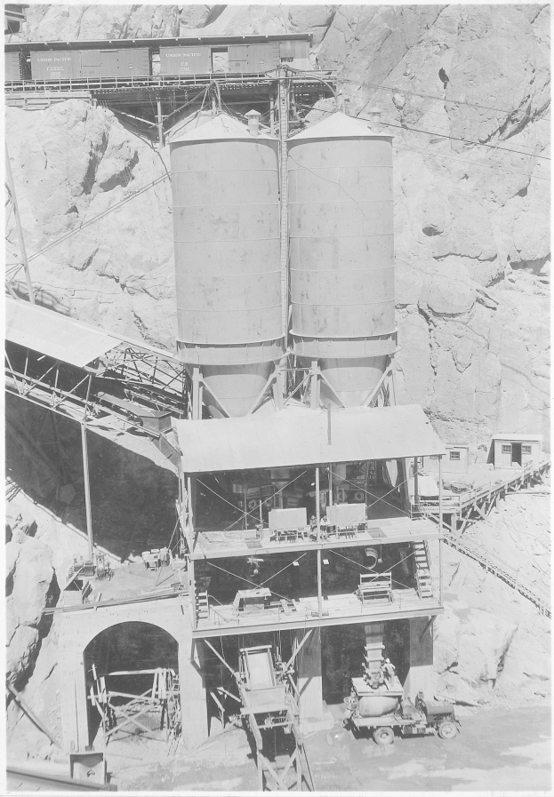 Schwarzes und weißes Foto eines Kohlebergwerks mit Fahrzeugen, einer Brücke, Gebäuden im Vordergrund und Bergen im Hintergrund, einschließlich Text unten.