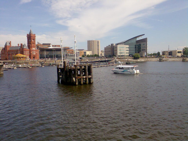 Ein Schloss, Gebäude, ein Boot, Wasser, Sand und Bäume sind im Bild zu sehen.