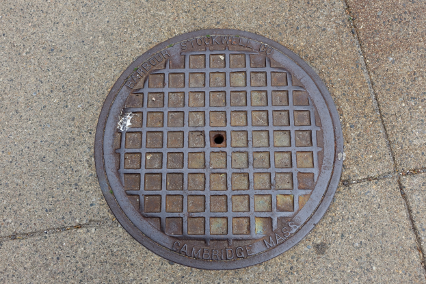Ein rundes Metallgullideckel auf einem Stadtweg mit eingravierter Text.