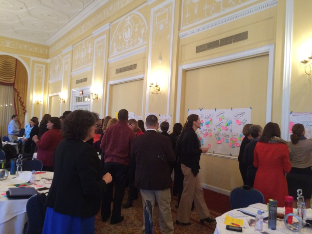 Eine Gruppe von Menschen, die Plakate und Charts an einer Wand in einem Gebäude betrachten, das wie ein Kunstmuseum aussieht.