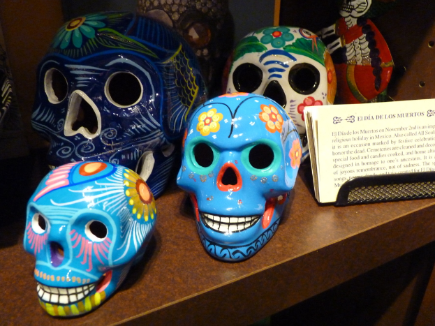 Ein Tisch mit verschiedenen farbig bemalten Schädeln neben Papieren mit einer Notiz.