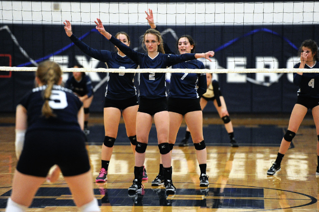 Drei Mädchen bei einem Volleyballspiel auf dem Feld stehend, eine Netz vor ihnen und ein Zaun im Hintergrund.