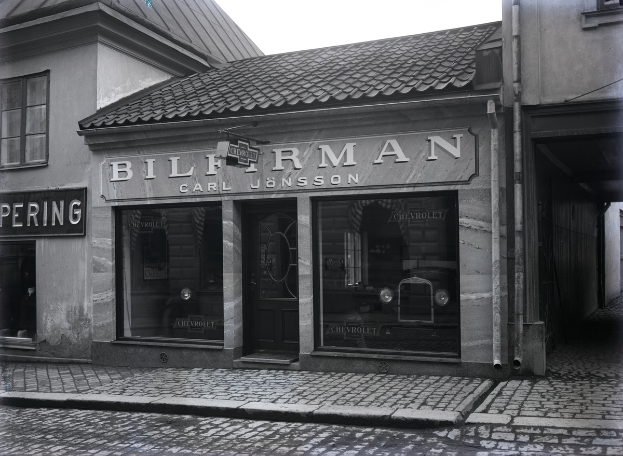 Ein Schwarz-Weiß-Foto eines Gebäudes mit einer 'Bilferman'-Aufschrift, Fenstern, einer Tür und Tafeln mit Text, sowie einer Straße unten.