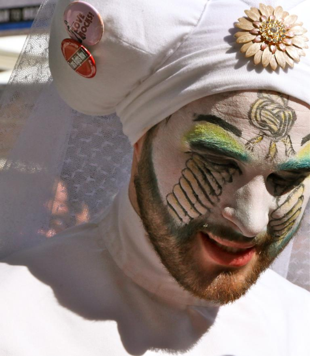Ein Mann mit Gesichtsbemalung und einer Mütze mit Text, der vor einem Stoffhintergrund steht.