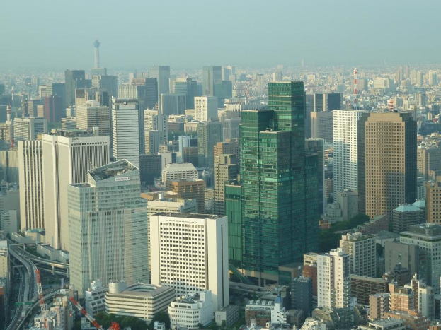 Eine Luftaufnahme einer Stadt mit zahlreichen Gebäuden in der Mitte, Straßen mit Fahrzeugen unten und Himmel oben.
