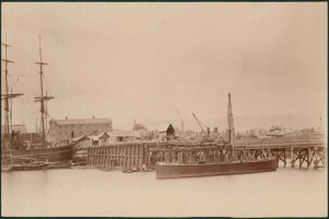 Eine Szene mit Wasser, Booten, Gebäuden, Strommasten und einem Himmel im Hintergrund.