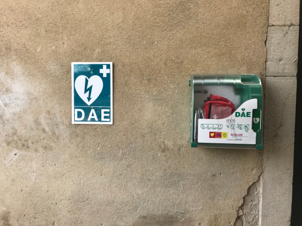 Eine Wand mit einem Schild, auf dem "Dae" steht und einem Defibrillatorgehäuse mit einer Tasche.