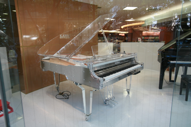 Zwei Klaviere, eines weiß und eines schwarz, vor einer braunen Wand positioniert.