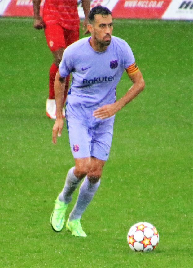 Ein Fußballspieler in einem Sportoutfit und Fußballschuhen ist im Einsatz auf dem Feld, mit einer Texttafel im Hintergrund.