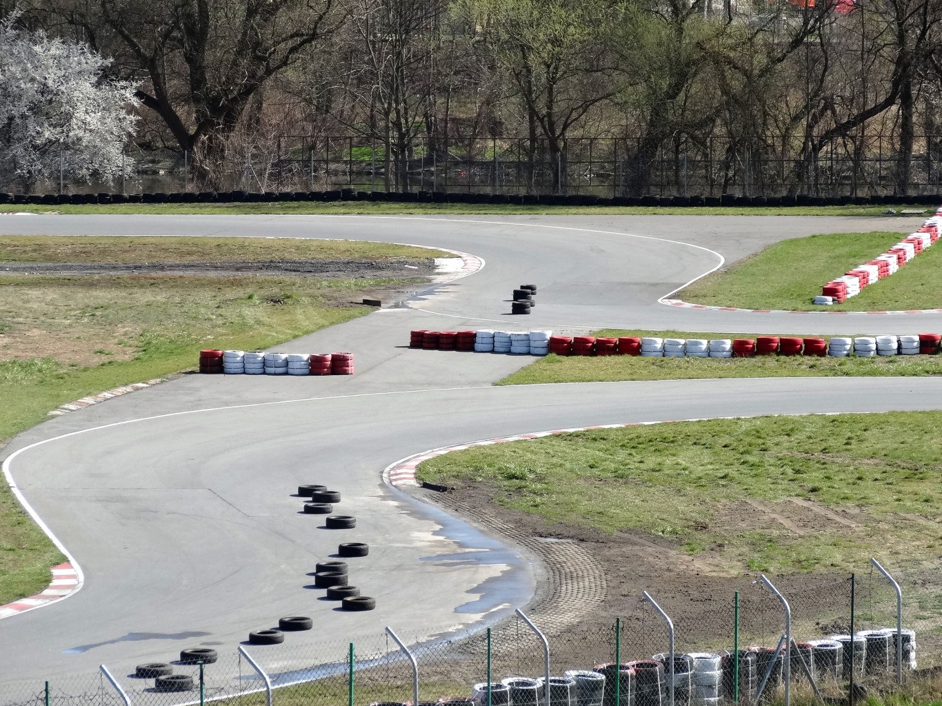 Rennstrecke voller Reifen, umgeben von Gras und Maschendrahtzaun, mit Bäumen im Hintergrund.