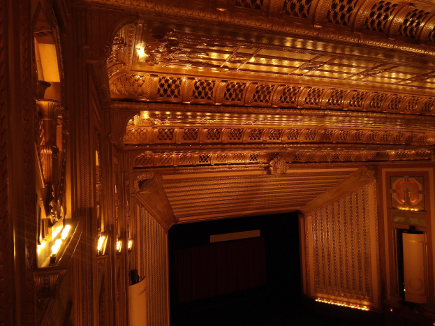 Das Innere eines Theaters mit dunklem Hintergrund, beleuchtet von links und rechts, mit einer kunstvoll gestalteten Decke.