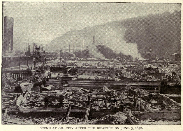 Schwarzes und weißes Foto einer Stadt nach einer Katastrophe am 5. Juni 1892, das beschädigte Gebäude, Mästäbe, Rauch und einen Hügel im Hintergrund zeigt.