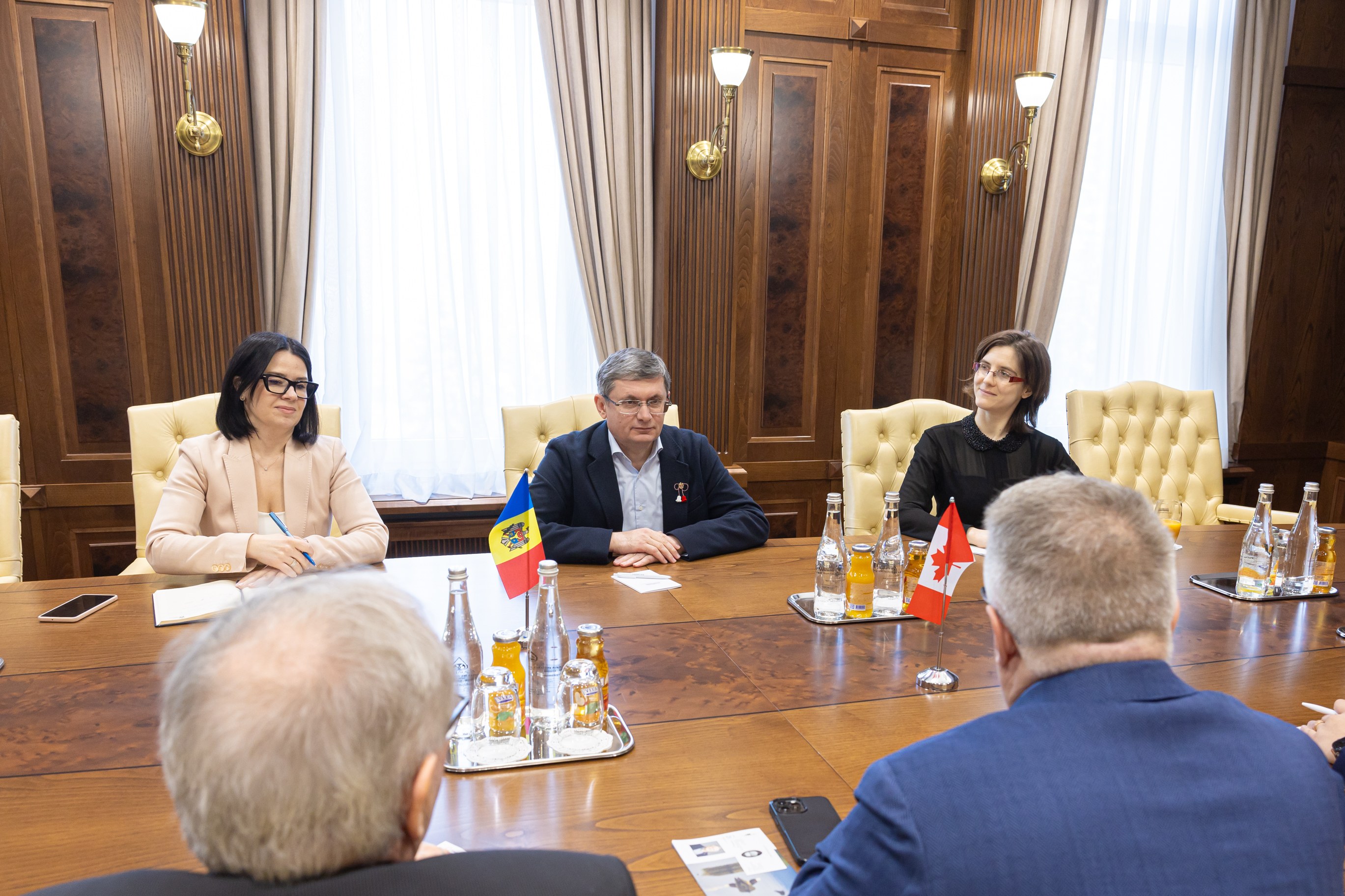 Eine Gruppe von Menschen, die um einen Holztisch in einem formellen Setting sitzen und mit EU-bezogenen Materialien und Gegenständen auf dem Tisch diskutieren.