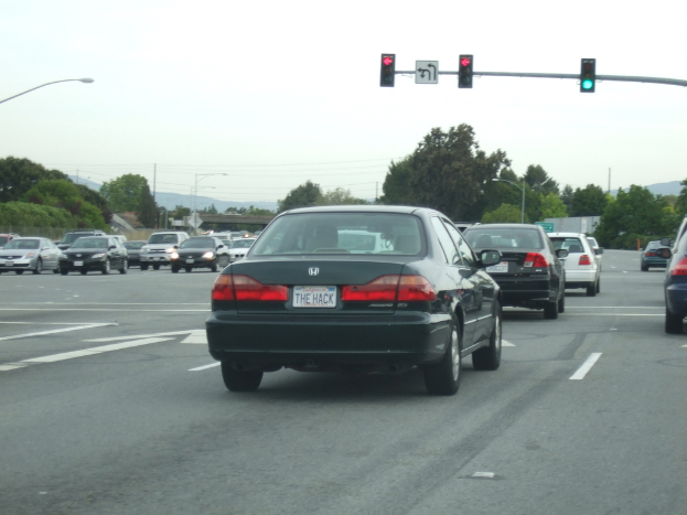 Eine vielbefahrene Straße mit zahlreichen Fahrzeugen, drei Strommasten und einer Ampel auf der rechten Seite unter einem klaren Himmel.