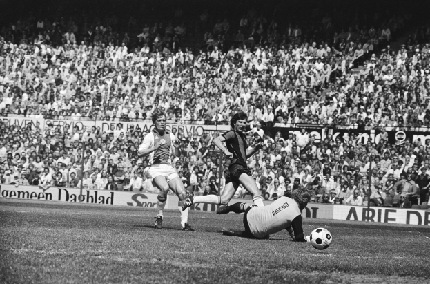 Schwarzes Foto von Männern beim Fußballspielen auf einem Feld mit Zuschauern im Hintergrund und einer "Bundesliga 1978-79 Ajax 1-1 Hannover 96"-Tafel.