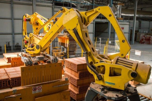 Großes industrielles Lagerhaus mit gestapelten Kisten, Kränen an der Decke, Zaun, Pfählen und einer fernen Wand in einer Fertigungsumgebung.