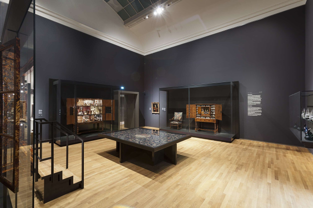 Ein unordentlicher Raum mit Glaswänden, einem Bodentisch, einer Treppe, Schränken mit Gegenständen, gerahmten Fotos an der Wand und Deckenleuchten, Teil des Museums of Fine Arts in New York City.