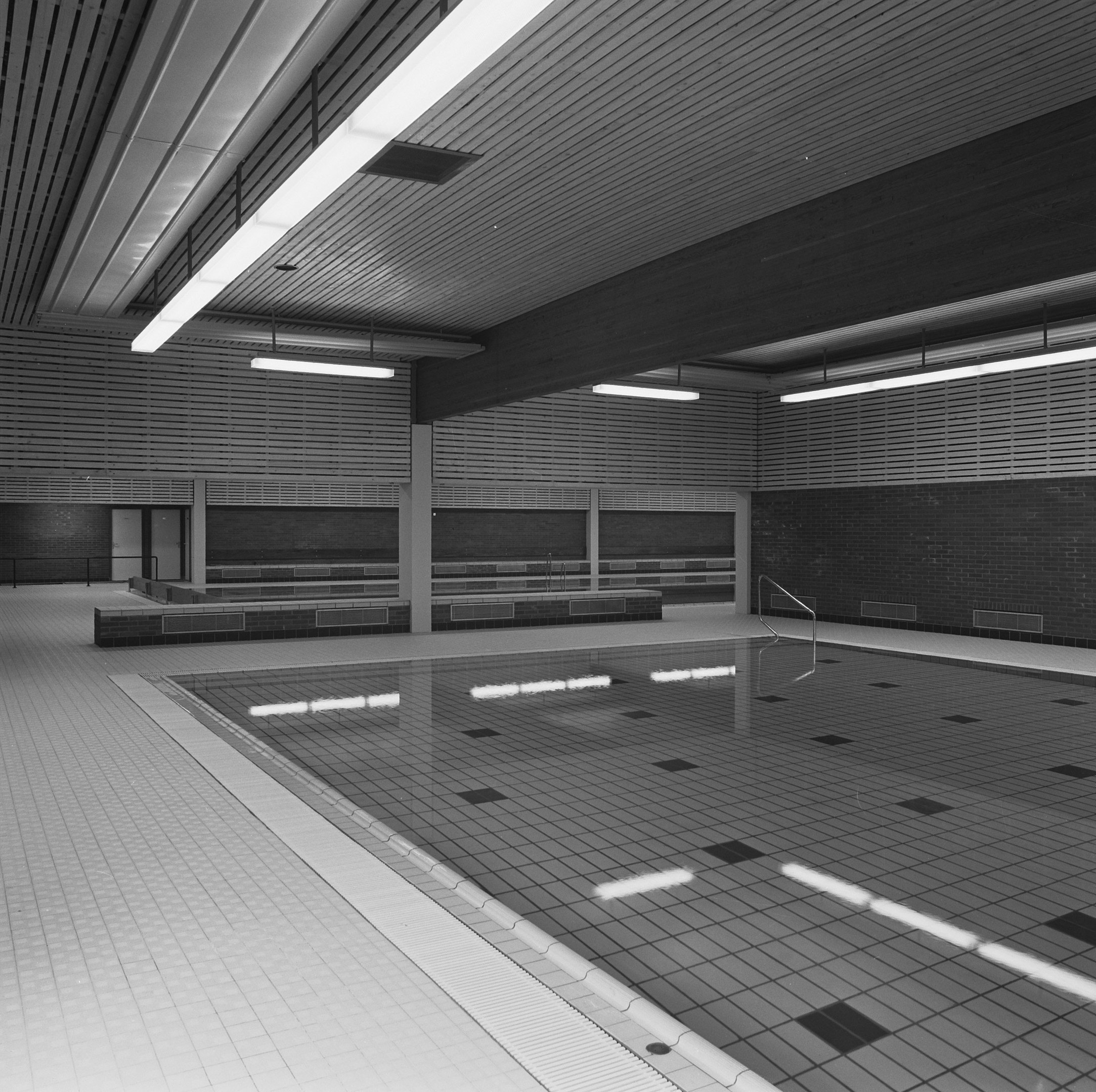 Innenpool mit klarem Wasser, gefliestem Boden und Wänden, Deckenbeleuchtung und einigen umgebenen Gegenständen in einem großen, friedlichen Gebäude.