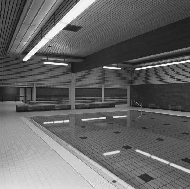 Innenpool mit klarem Wasser, gefliestem Boden und Wänden, Deckenbeleuchtung und einigen umgebenen Gegenständen in einem großen, friedlichen Gebäude.