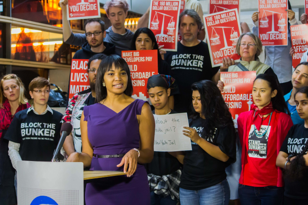 Eine Black Lives Matter-Aktivistin, die vor einer Menge mit Schildern spricht, mit einem Mikrofon und anderen Gegenständen im Hintergrund.