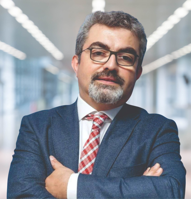 Ein Mann im Anzug und Krawatte mit verschränkten Armen, der eine Brille trägt und vor einem unscharfen Hintergrund steht, identifiziert als der neu ernannte Marketingchef.