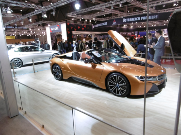 Ein stylischer schwarzer BMW i8 Roadster mit Chromakzenten auf der Frankfurt Motor Show umgeben von formell gekleideten G├Ąsten.