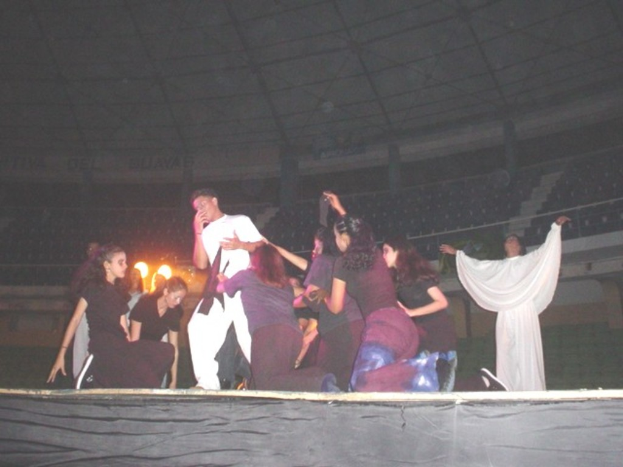 Eine Gruppe performs auf einem Podium mit Sitzplätzen, Grills und einem Schuppen im Hintergrund.