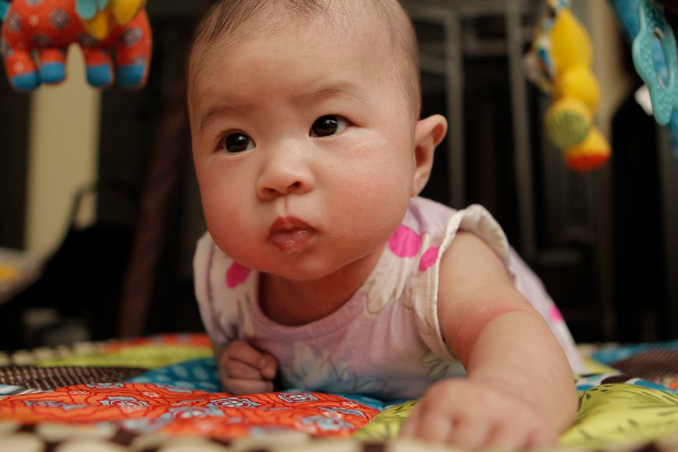 Ein Baby liegt auf einem Bettlaken mit ein paar Spielzeugen oben drauf, und ein unscharfer Hintergrund.