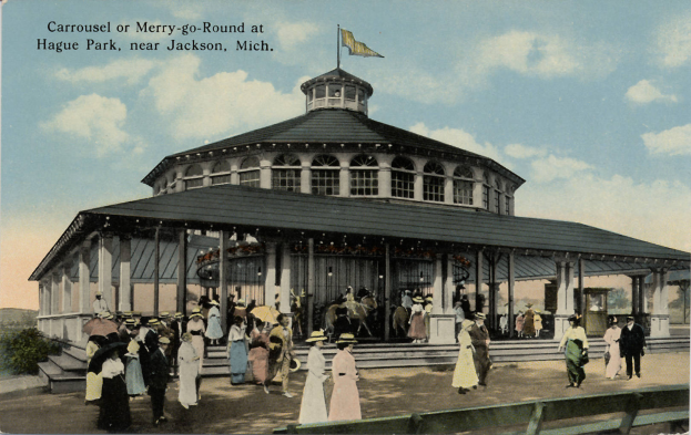 Eine alte Postkarte zeigt ein Karussell im Hague Park, Jackson, Michigan, mit Menschen, einige halten Schirme, ein Gebäude mit Säulen und einer Flagge, Bäume und einen bewölkten Himmel, mit Text oben.