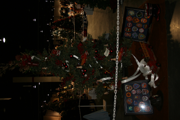 Ein Weihnachtsbaum mit Geschenken, Rahmen und Spielzeug auf einer Plattform, mit Menschen, Bäumen und Dekorationen im Hintergrund.