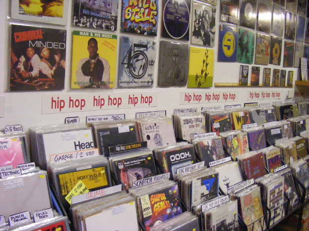 Ein Metallständer mit Büchern und optischen Disc-Cases, jeweils verziert mit Postern mit Text und Bildern, sowie zusätzlichem Text auf Papieren an der Wand in der Mitte.