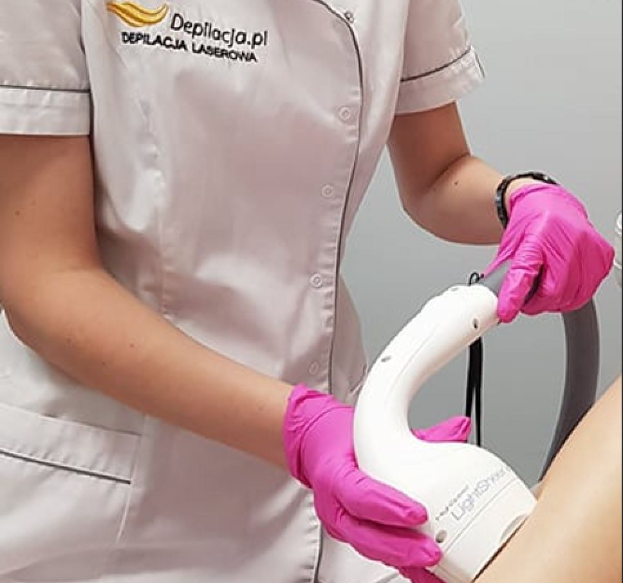 Eine Frau in einem weißen Hemd und pinken Handschuhen bedient eine weiße Laser-Haarentfernungsmaschine an ihrer Haut, während sie vor einer Wand steht.