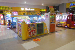Ein großer Arcade-Raum mit verschiedenen Arten von Arcade-Automaten, Deckenleuchten und einer Hintergrundwand in einer Vergnügungsparkanlage.
