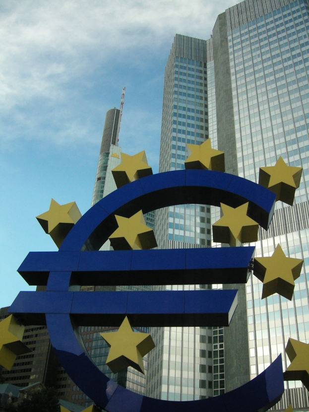 Euro-Zeichen vor dem Hauptquartier der Europäischen Zentralbank in Frankfurt, Deutschland, mit Bäumen und bewölktem Himmel im Hintergrund.