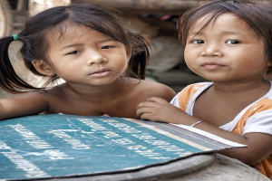 Zwei Kinder sind zu sehen, wobei das Kind auf der rechten Seite Kleidung trägt, ein Haarband hält und ein Papierblatt hält, mit einem unscharfen Hintergrund.