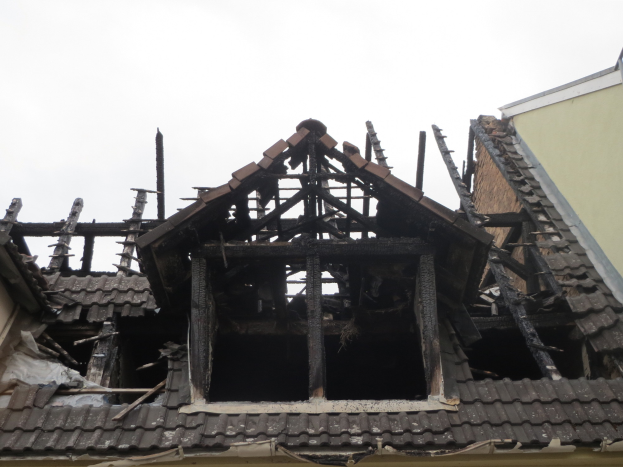 Ein Gebäude mit einem teilweise zerstörten Dach, das Brandschäden aufweist, mit Schutt in der Umgebung und dem Himmel im Hintergrund.