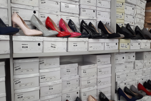 Ein Regal voller verschiedener Schuharten in Kartons, jeweils mit einem Preisschild, und Kartonagen auf der rechten Seite.