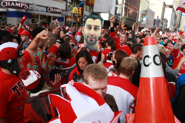Eine Gruppe von Menschen vor Gebäuden stehend, mit einer Ampel und einer Flagge im Hintergrund.