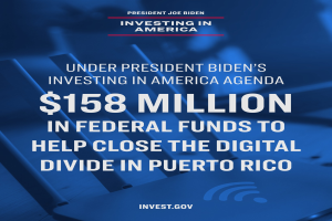 Ein Plakat mit Text über das Investing in America-Programm von Präsident Biden und 158 Millionen Dollar Bundesmittel für die digitale Kluft in Puerto Rico, mit einem Laptop, einem Stapel Papiere und einem Kaffeebecher auf einem Tisch davor.