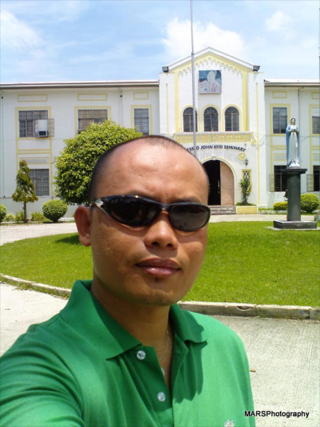 Eine Person in einem grünen Kleid steht vor einem Gebäude mit Türen, Bussen und einer Statue auf dem Rasen.