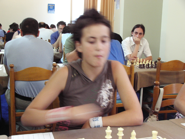 Ein Raum mit Menschen an Tischen beim Schachspielen, eine Vorhangwand mit einem Foto in der Ecke.