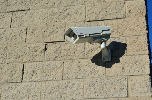 Eine Überwachungskamera, die an der Seite eines Gebäudes montiert ist und einen hellblauen Himmel im Hintergrund zeigt.