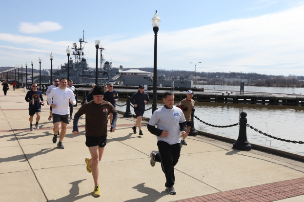 Eine volle Br√ľcke mit Menschen, die laufen, Laternenpf√§hle, Wasser, Berge und Geb√§ude im Hintergrund.