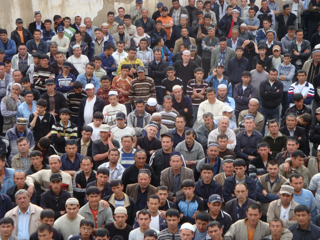 Eine große Gruppe von Menschen, einige mit Mützen, vor einem Gebäude mit einer Wand im Hintergrund.
